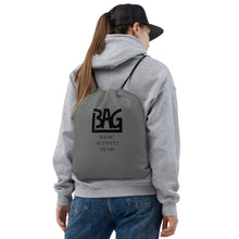 Load image into Gallery viewer, Person wearing a grey drawstring bag with B,A,G Logo combined with &#39;Basic Activity Gear&#39; text on it
