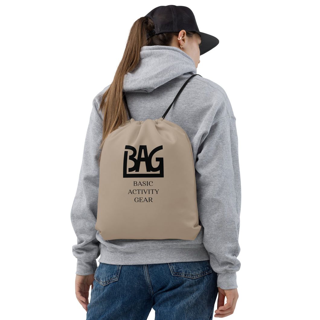 Person wearing a khaki drawstring bag with B,A,G Logo combined with 'Basic Activity Gear' text on it