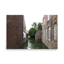 Load image into Gallery viewer, Narrow canal flanked by brick buildings with trees in the background
